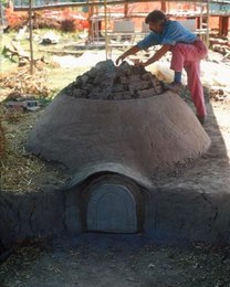 Final phase in building a pottery kiln. The structure comprises a circular combustion chamber with a protruding dome in compacted clay and vegetable fibre. The mouth takes in air, which is funnelled through a chimney at the rear to favour and control the flow.